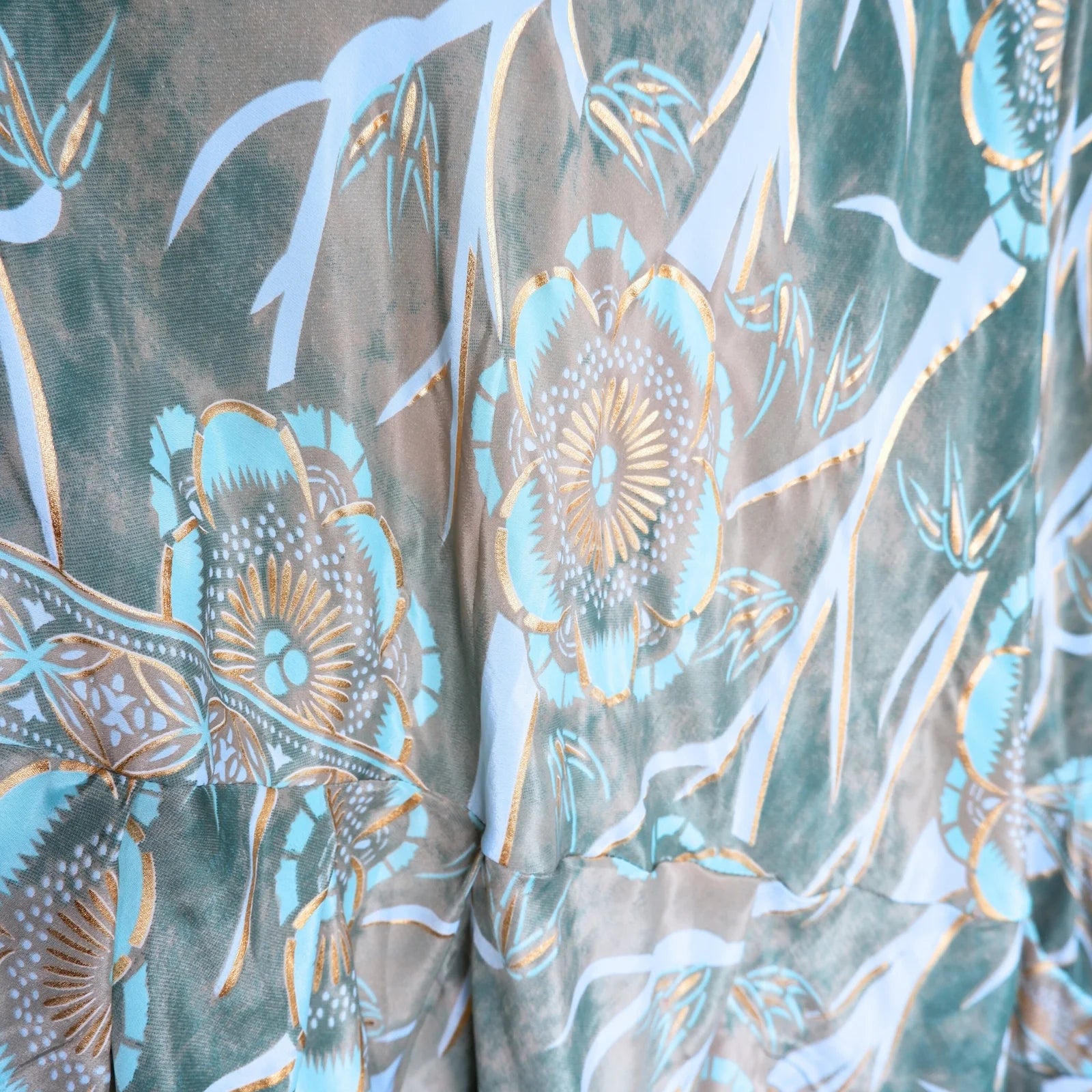 Close-up of fabric with floral pattern in teal, gold, and brown.